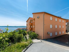 A multi-story building with balconies, a paved area in front, and a view of the sea. - Omega Cert / HR-09851-01 by Interhome (Crikvenica)