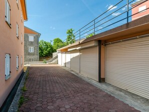 A paved walkway between buildings with closed shutters, a clear sky, and a visible staircase. - Omega Cert / HR-09851-01 by Interhome (Crikvenica)