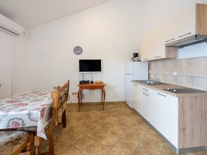 Uma cozinha compacta com uma mesa de jantar, uma televisão e armários brancos.