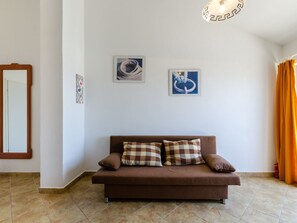 Uma sala de estar com um sofá marrom, duas quadros emoldurados, um espelho e uma janela com cortinas.