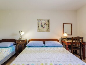 Quarto com duas camas, uma escrivaninha e uma cadeira. Há abajures nas mesas de cabeceira.