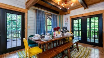 A dining area with a wooden table set for four, a bench, and a view of the outdoors through large windows.