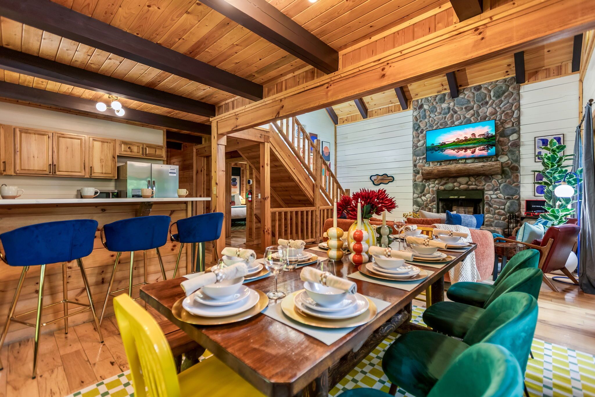 A wooden interior with a dining area set for a meal, a kitchen, and a living area with a stone fireplace.