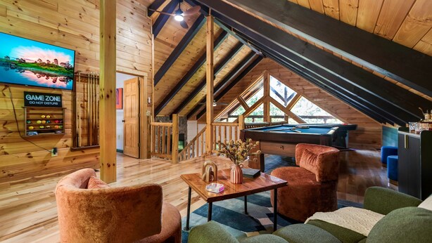 Una habitación acogedora con mesa de billar, paredes de madera, televisor y un letrero que dice 'GAME ZONE'.