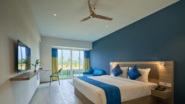 A modern hotel room with a large bed, a ceiling fan, a TV, and a view of the outdoors. - Ikshana Resort and Spa (Mawal)