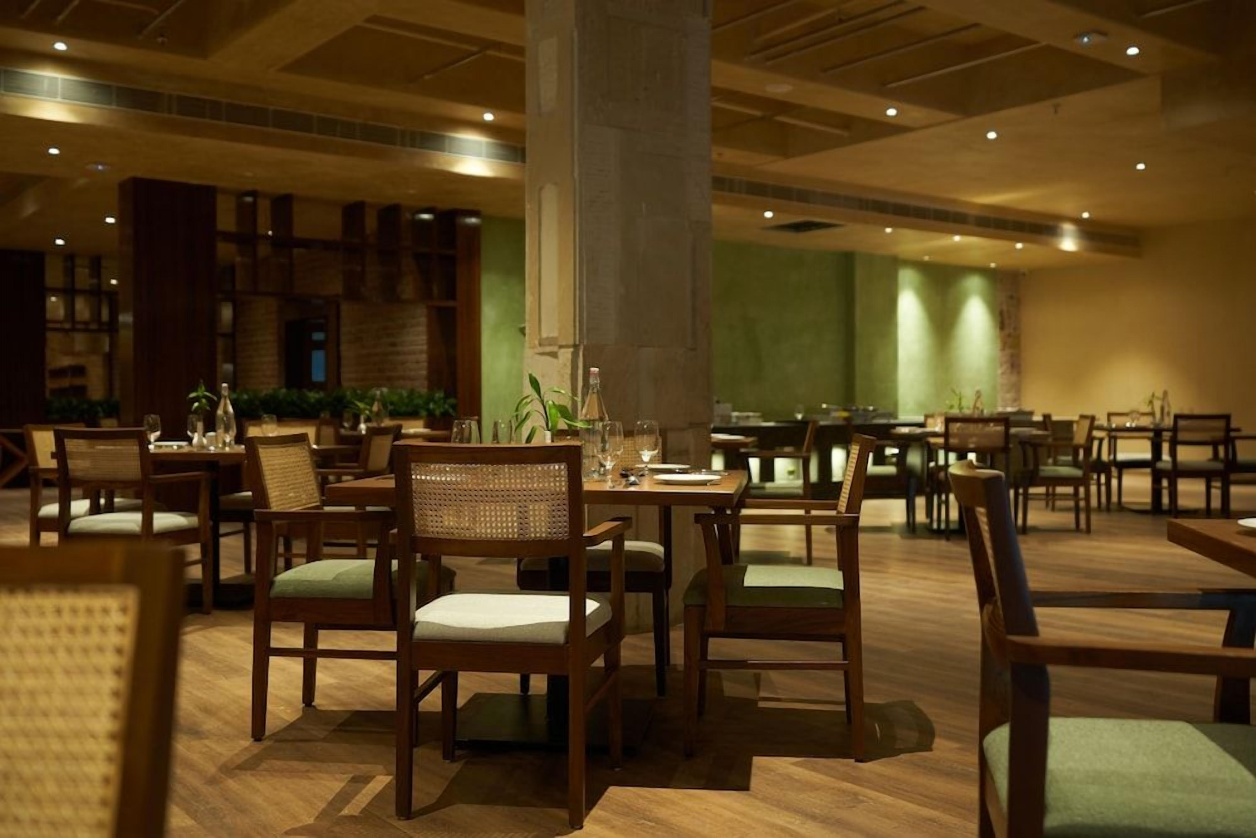 Un restaurant avec des meubles en bois, des chaises à coussins verts et un pilier central.
