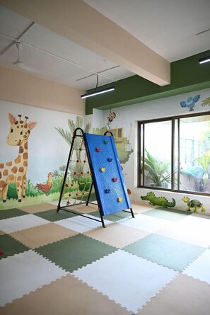 Zona de juegos con pared de escalar, un mural de jirafa y ventana con vista a follaje.