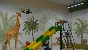A play area with a slide, climbing structure, and wall murals of animals. - Ikshana Resort and Spa (Mawal)