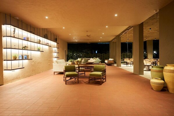 Un espacio interior amplio con una disposición de asientos, un estante de pared con objetos decorativos y vistas del exterior en la noche.