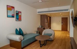 Una sala de estar con sofá, sillón, mesa de centro y una obra de arte en la pared.