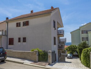 Ein zweistöckiges Gebäude mit weißer Fassade, rotem Ziegeldach und einem Balkon im zweiten Stock.