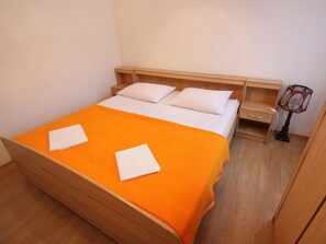 Ein Zimmer mit einem Einzelbett, einer orangefarbenen Tagesdecke, weißen Kissen, einem Holz-Kopfteil, einem Nachttisch und einer Lampe.
