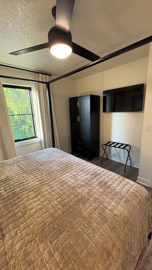 A bedroom with a bed, a ceiling fan, a wardrobe, a TV, and a window with curtains.