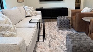 A living room with a sofa, ottoman, and a television on the wall.