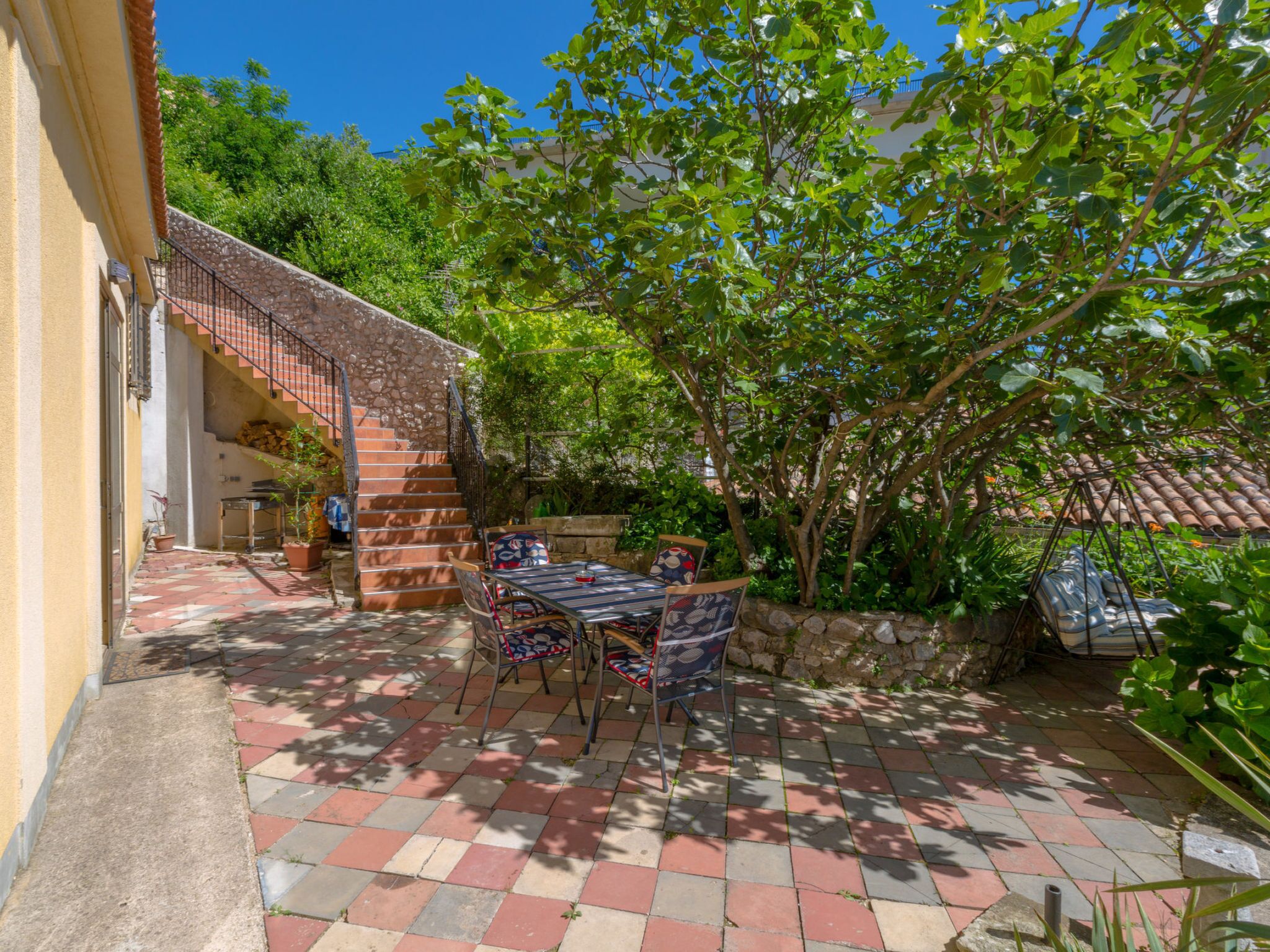A patio with a table and chairs, a stone staircase, and a view of the surrounding greenery.