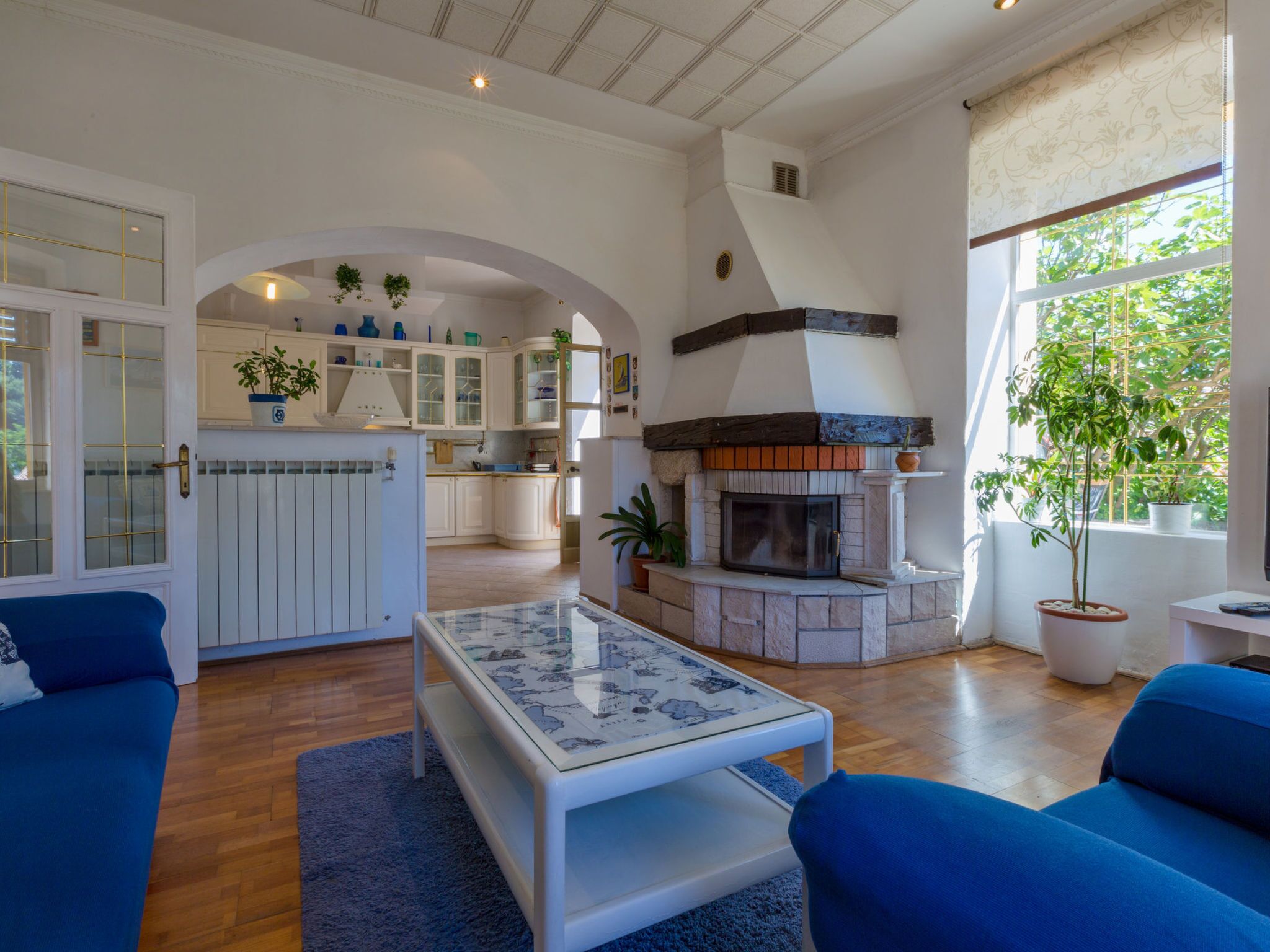 A spacious living area with a fireplace, blue sofas, and a kitchen in the background.