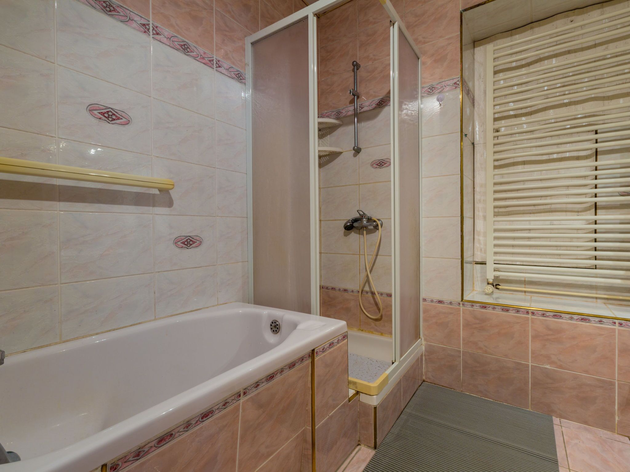 Un baño con bañera, ducha y ventana con persianas.