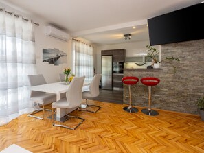 A modern kitchen with a stone backsplash, a dining area with a white table and chairs, and a bar area with red stools. - Monique / HR-11121-01 by Interhome (Crikvenica)
