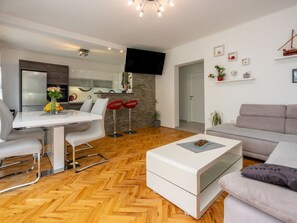 A modern living room with a sofa, a dining table with chairs, a coffee table, and a kitchen area with a TV. - Monique / HR-11121-01 by Interhome (Crikvenica)