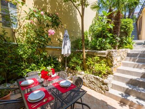 Un'area pranzo all'aperto con un tavolo imbandito per quattro persone, circondata da piante rigogliose e un muro di pietra.