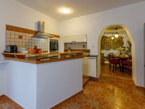 Een keuken met een centraal eiland, een eethoek met een stenen muur en een betegelde vloer.