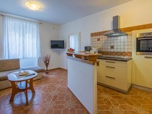 Una cucina compatta con forno a incasso, TV a schermo piatto e zona pranzo con divano e tavolo.