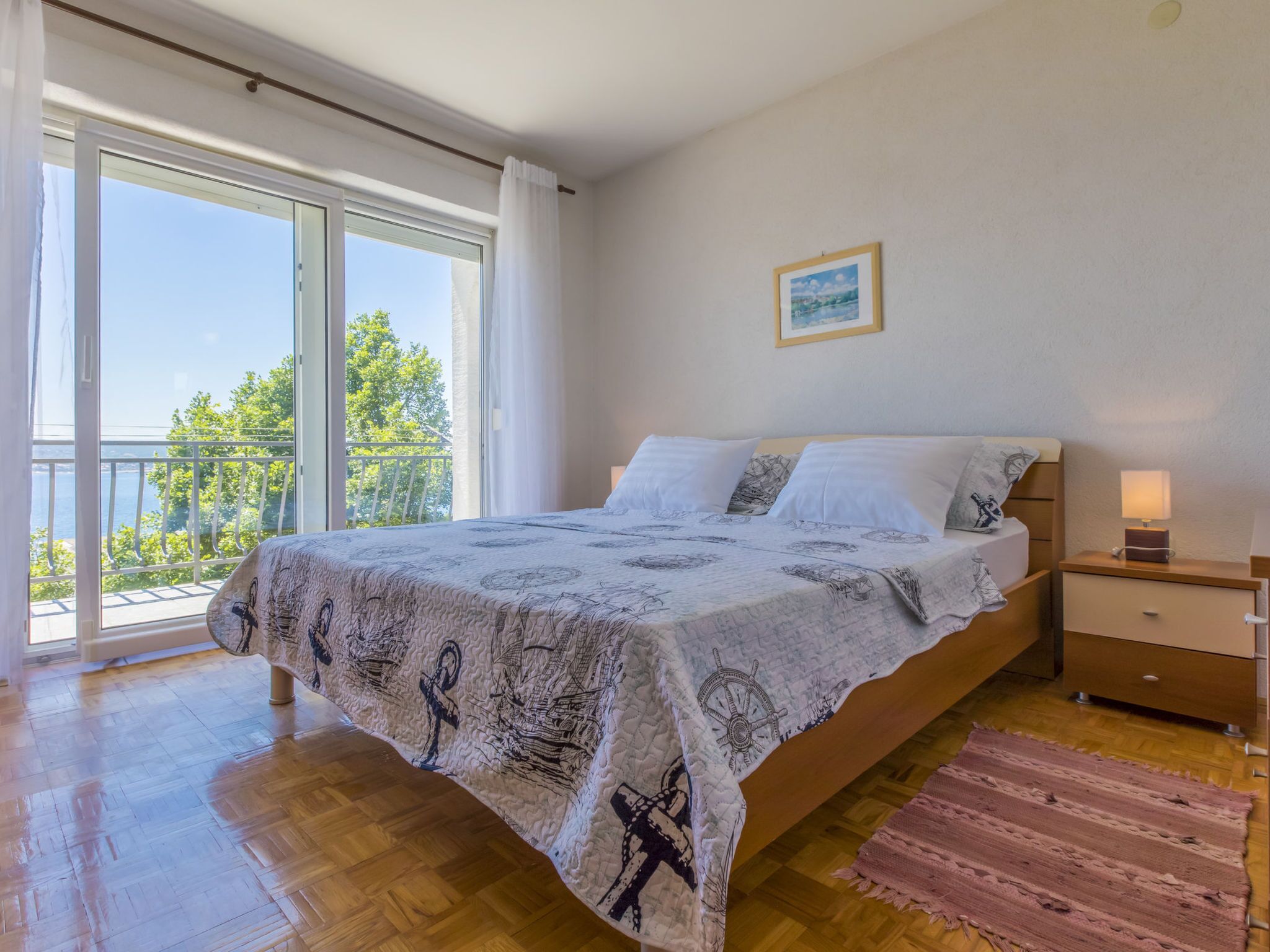 Un dormitorio con cama, mesita de noche, lámpara de noche, ventana con cortinas y vistas al exterior.