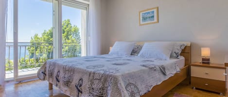Un dormitorio con cama, mesita de noche, lámpara de noche, ventana con cortinas y vistas al exterior.