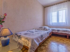 Une chambre avec deux lits, une table de chevet, une lampe et une fenêtre avec des rideaux légers.
