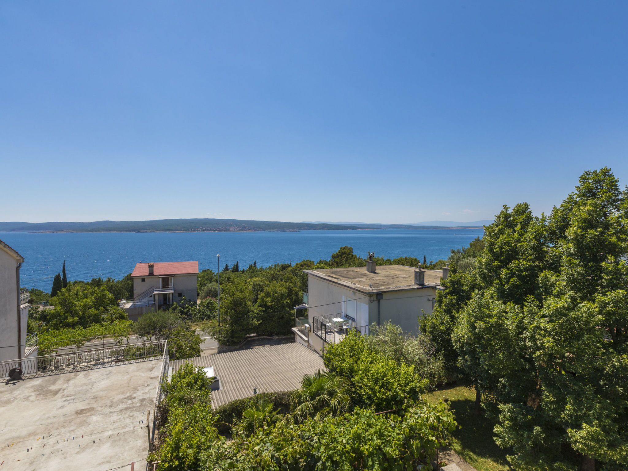 Zona residencial con vistas al mar, casas de techo rojo y abundante vegetación.