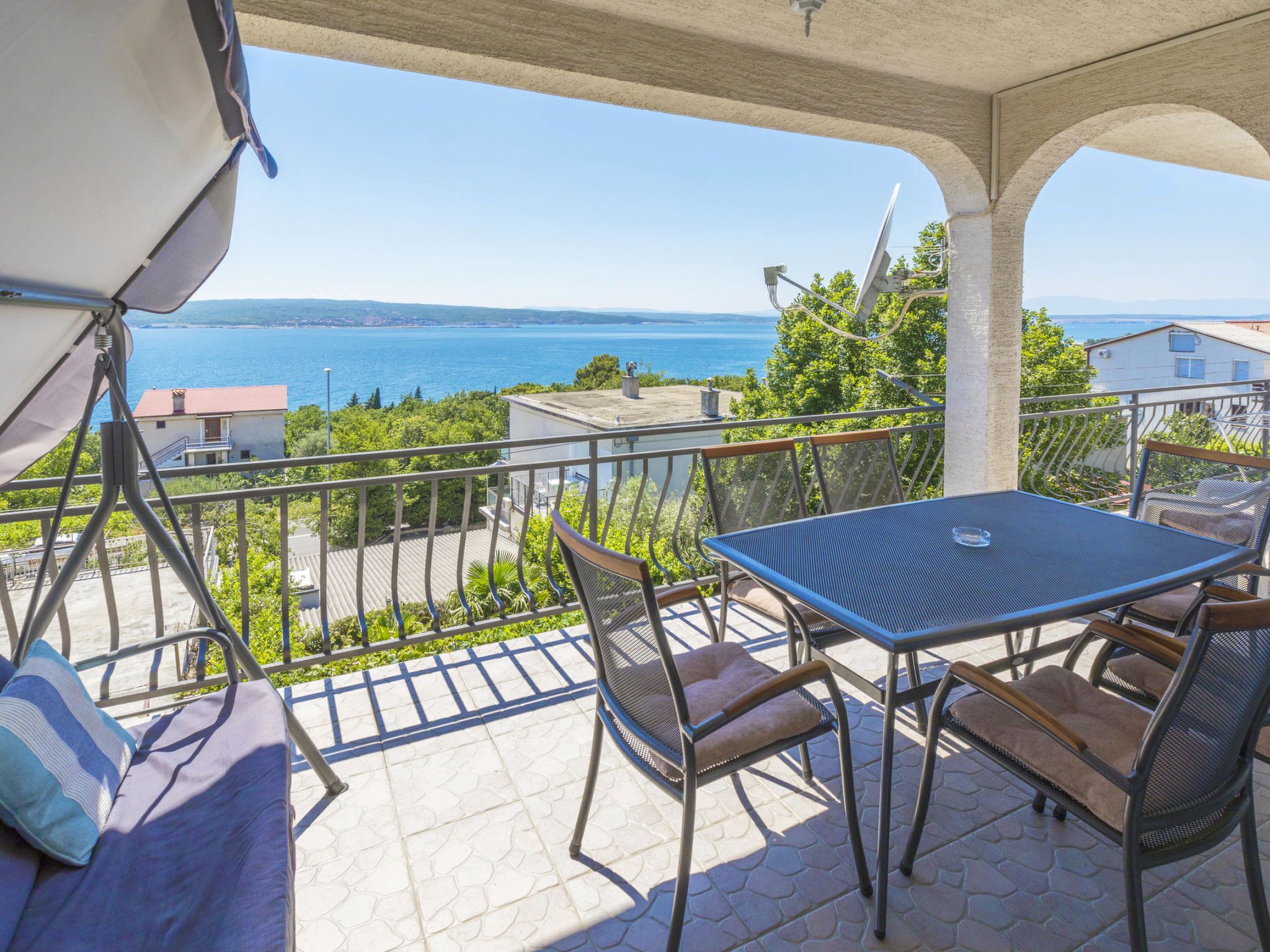A balcony with a table and chairs, overlooking a body of water and a distant coastline.