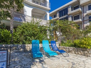A poolside area with lounge chairs, a warning sign, and a building with balconies. - KOSTRENCIC 3 / HR-09101-04 by Interhome (Crikvenica)