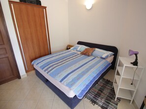 A bedroom with a bed, a nightstand, a wardrobe, and a shelf with a lamp. - KOSTRENCIC 3 / HR-09101-04 by Interhome (Crikvenica)