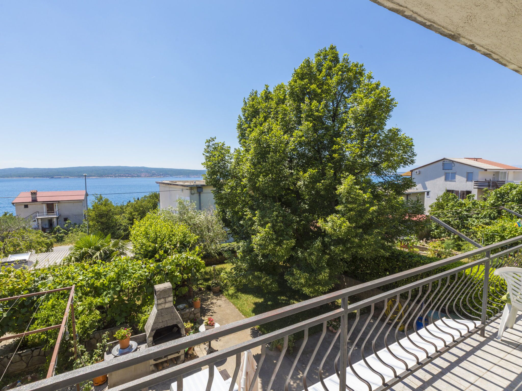 A balcony with a view of a tree, a stone oven, and a body of water.