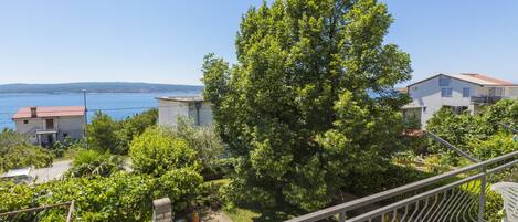 A balcony with a view of a tree, a stone oven, and a body of water.