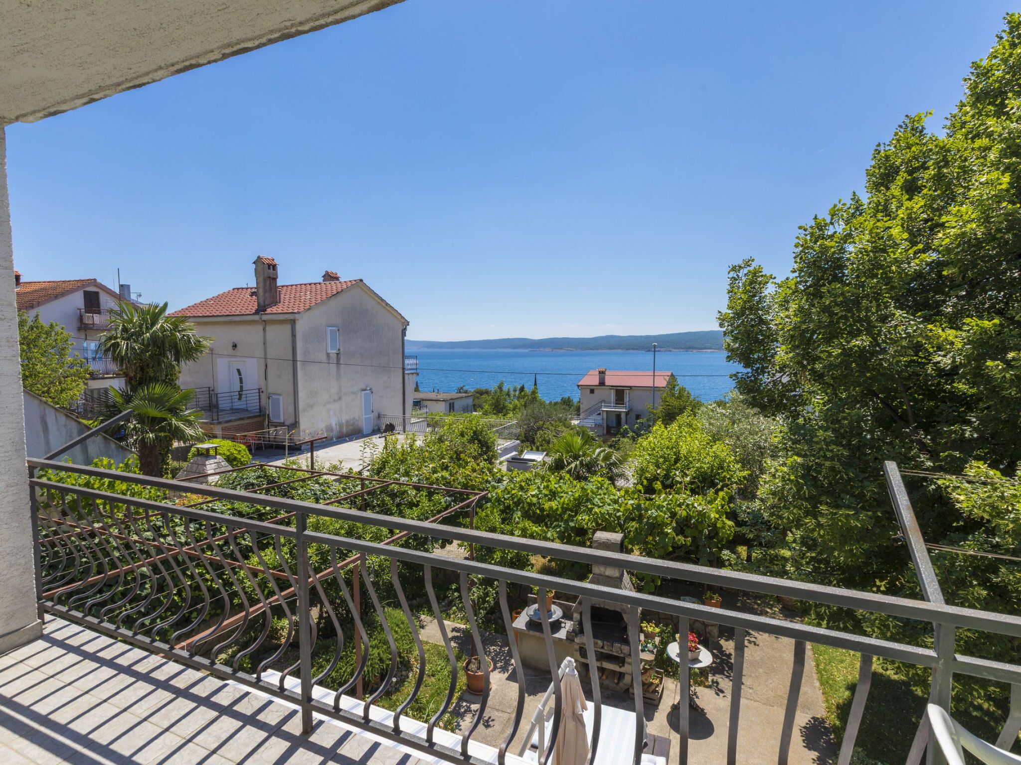 Un balcón con vista al mar, casas y vegetación.