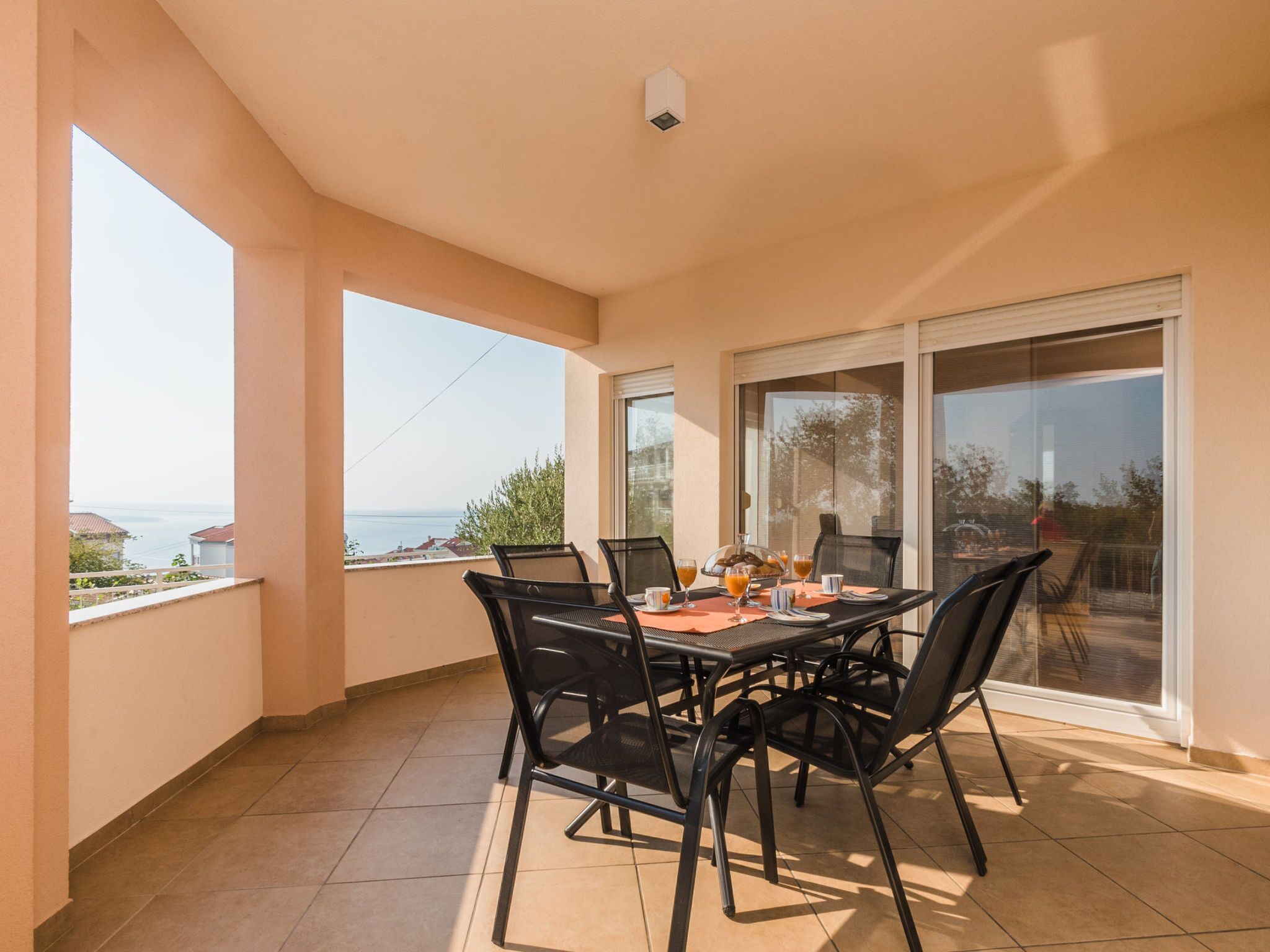 A balcony with a table set for breakfast, chairs, and a view of the sea.
