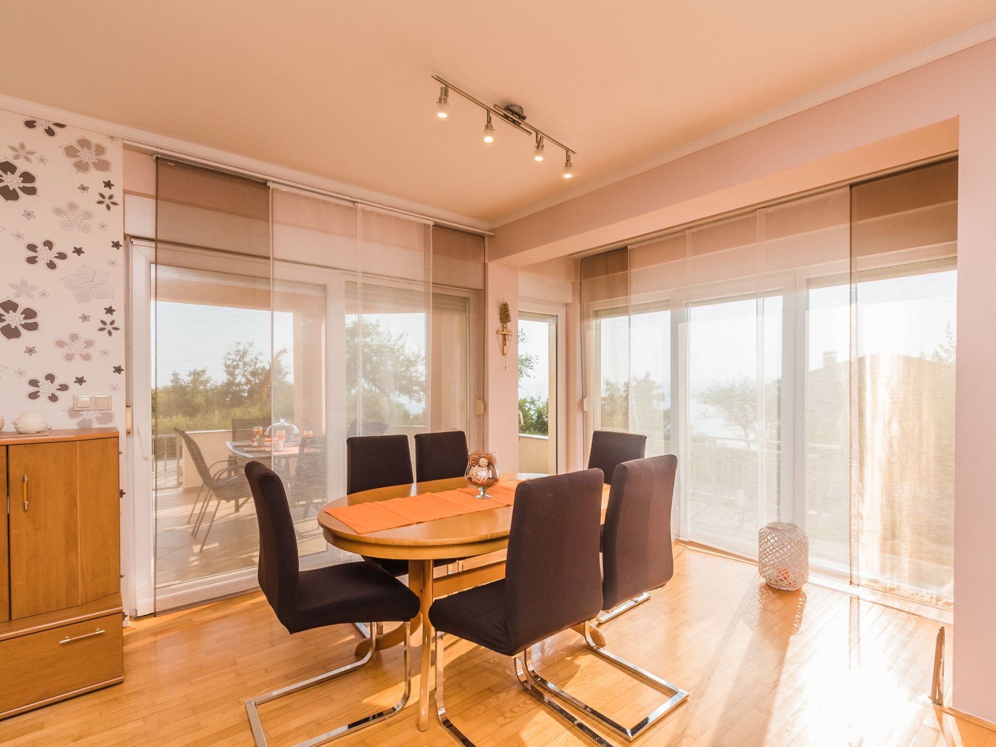 Un coin repas comprenant une table ronde, six chaises et une vue sur l’extérieur grâce à de grandes fenêtres.