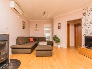 Ein Wohnzimmer mit einer Couch, Hocker, Kamin, Fernsehschrank und einem Blumentopf.