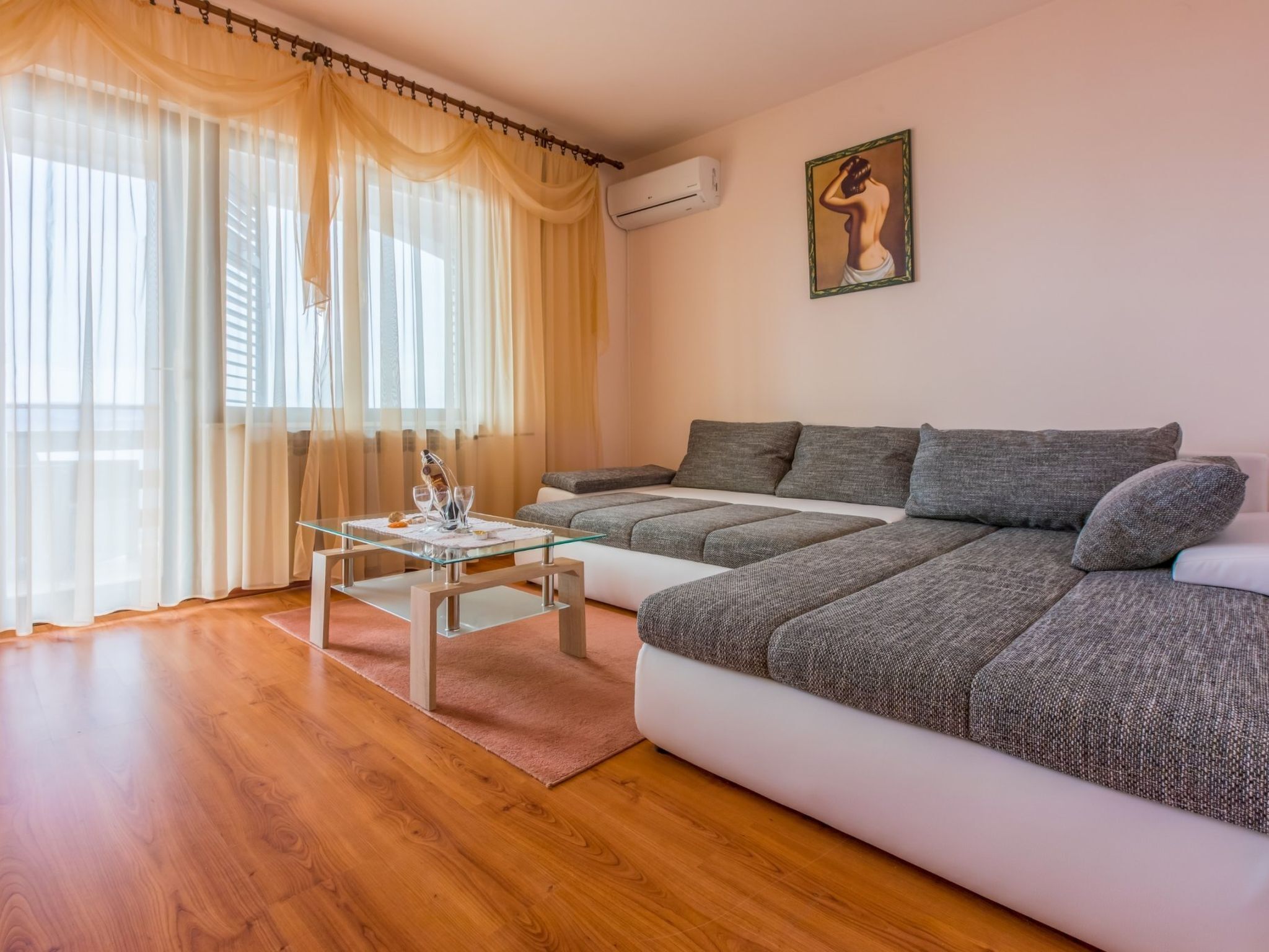 A modern living room with a sofa, a glass coffee table, and sheer curtains.