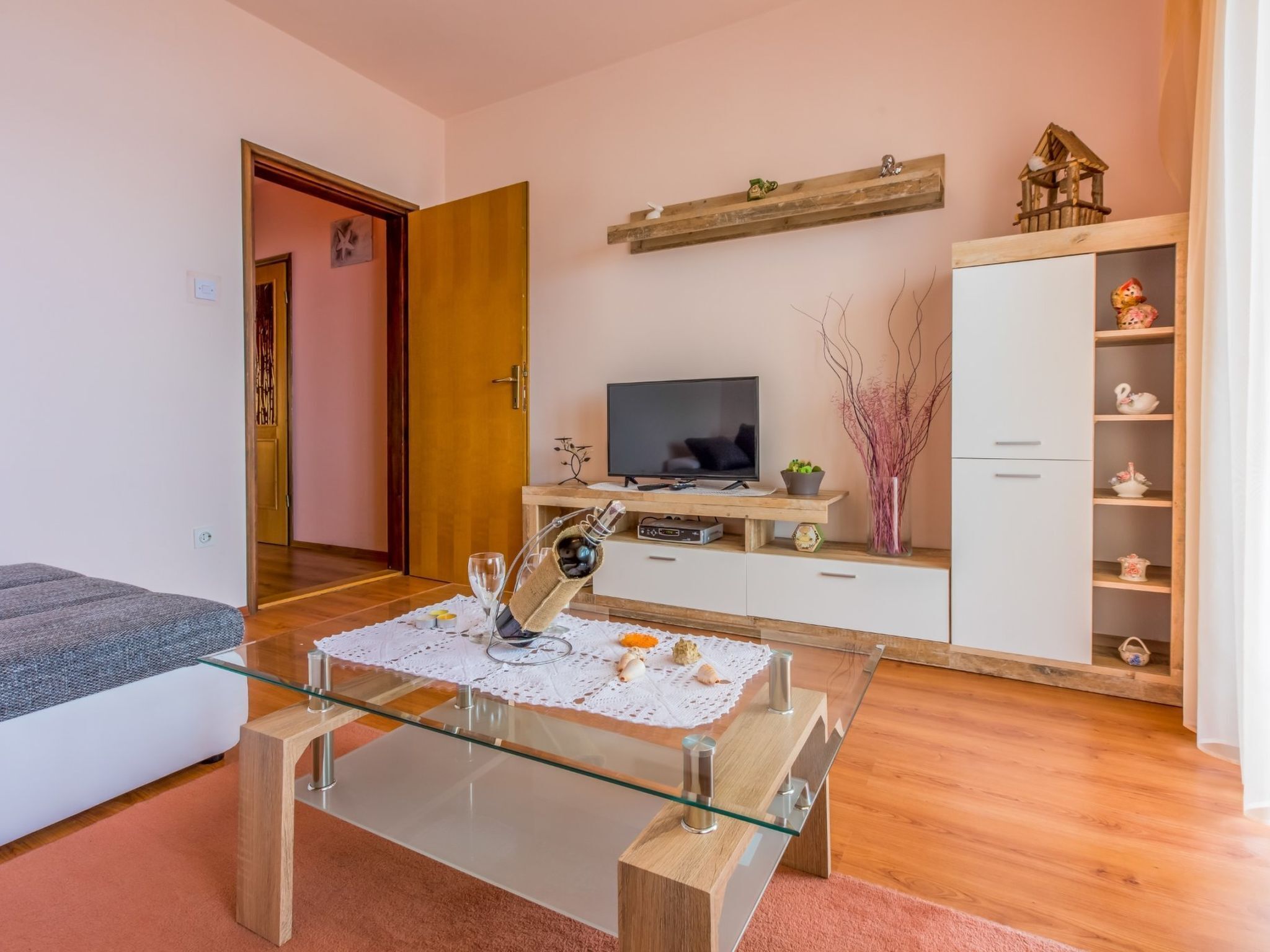 Een moderne woonkamer met een glazen salontafel, een televisie en een witte kast met decoratieve objecten.