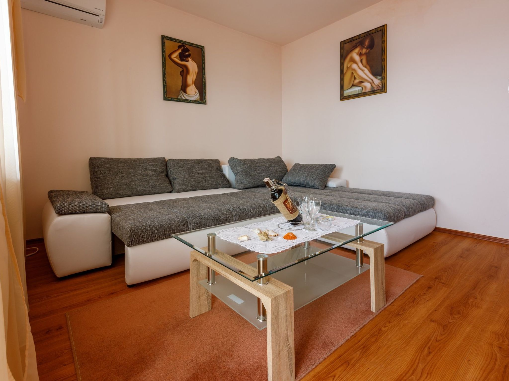 A modern living room with a grey sofa, a glass coffee table, and two paintings on the wall.