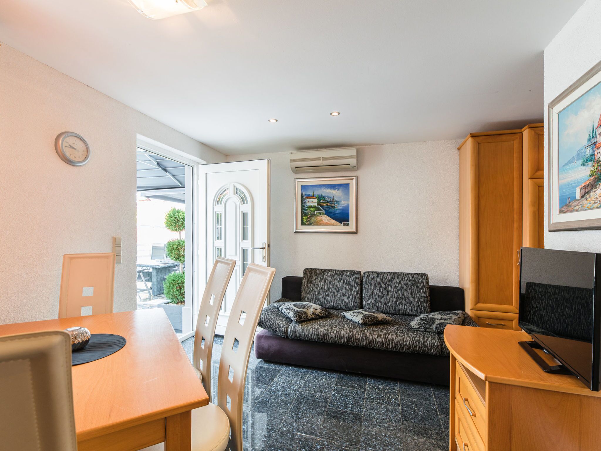 A compact living space with a dining table, chairs, a sofa, a television, and a painting on the wall.
