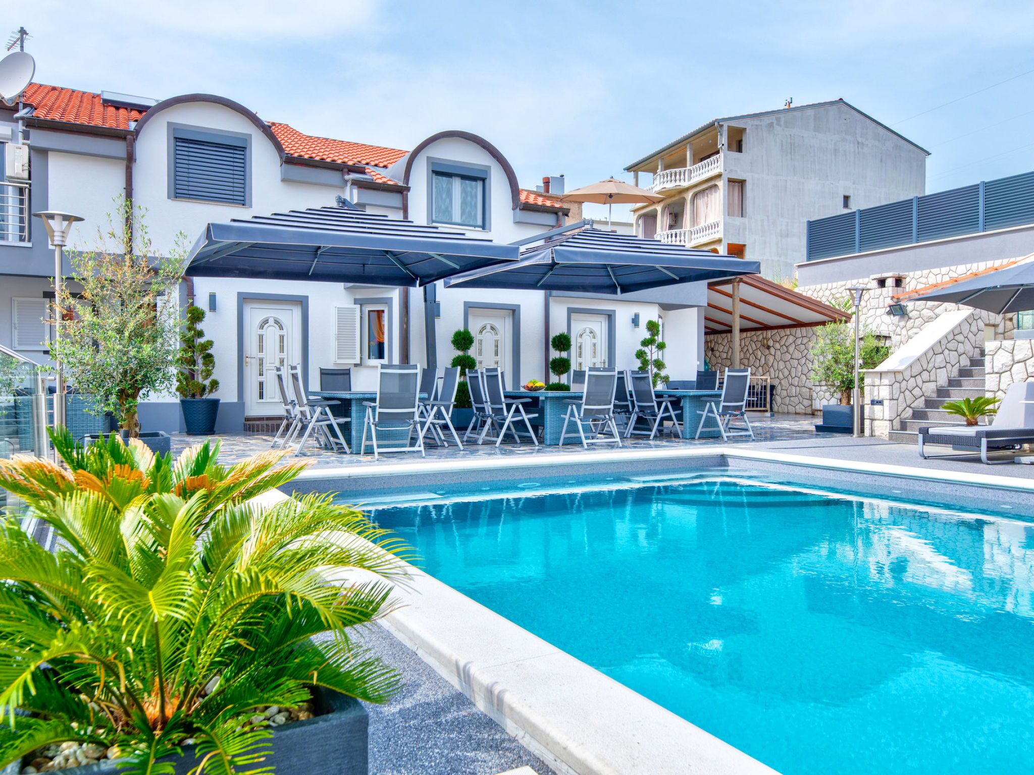 A swimming pool with lounge chairs and umbrellas, surrounded by buildings with stone walls and a tiled roof.