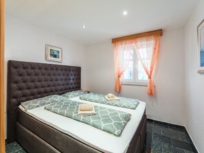 Ein Schlafzimmer mit einem großen Bett, zwei Kissen, einem Kopfteil, einem Fenster mit Vorhängen und einem Bild an der Wand.
