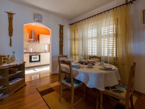 Un coin repas avec une table dressée pour quatre personnes, une cuisine en arrière-plan et une grande fenêtre avec des rideaux.