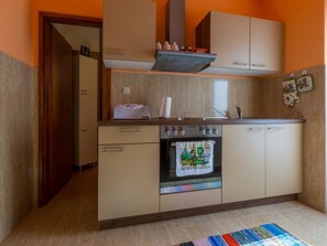 Une cuisine compacte équipée d’un four encastré, d’un four à micro-ondes et d’une cuisinière. On trouve un placard en bois au-dessus de la cuisinière et une petite fenêtre au-dessus du four.