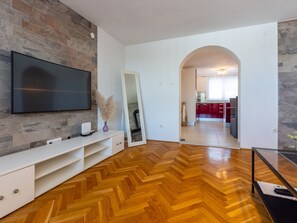 A modern living room with a flat-screen TV mounted on a stone wall, a white entertainment unit, and a herringbone wooden floor. - Sea View 1 prizemlje / HR-08682-05 by Interhome (Crikvenica)