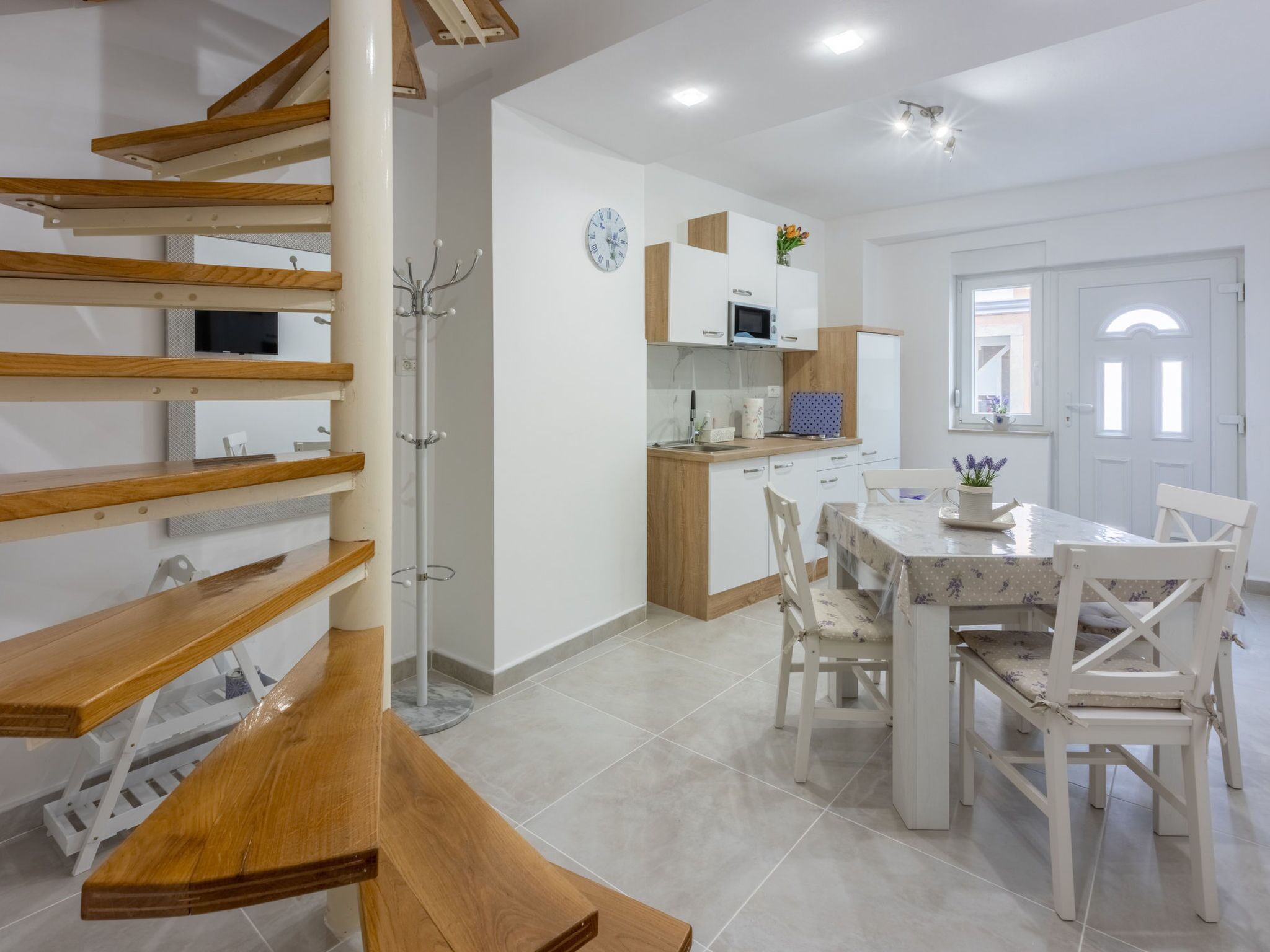 A modern kitchen with white cabinets, a microwave, and a clock on the wall.