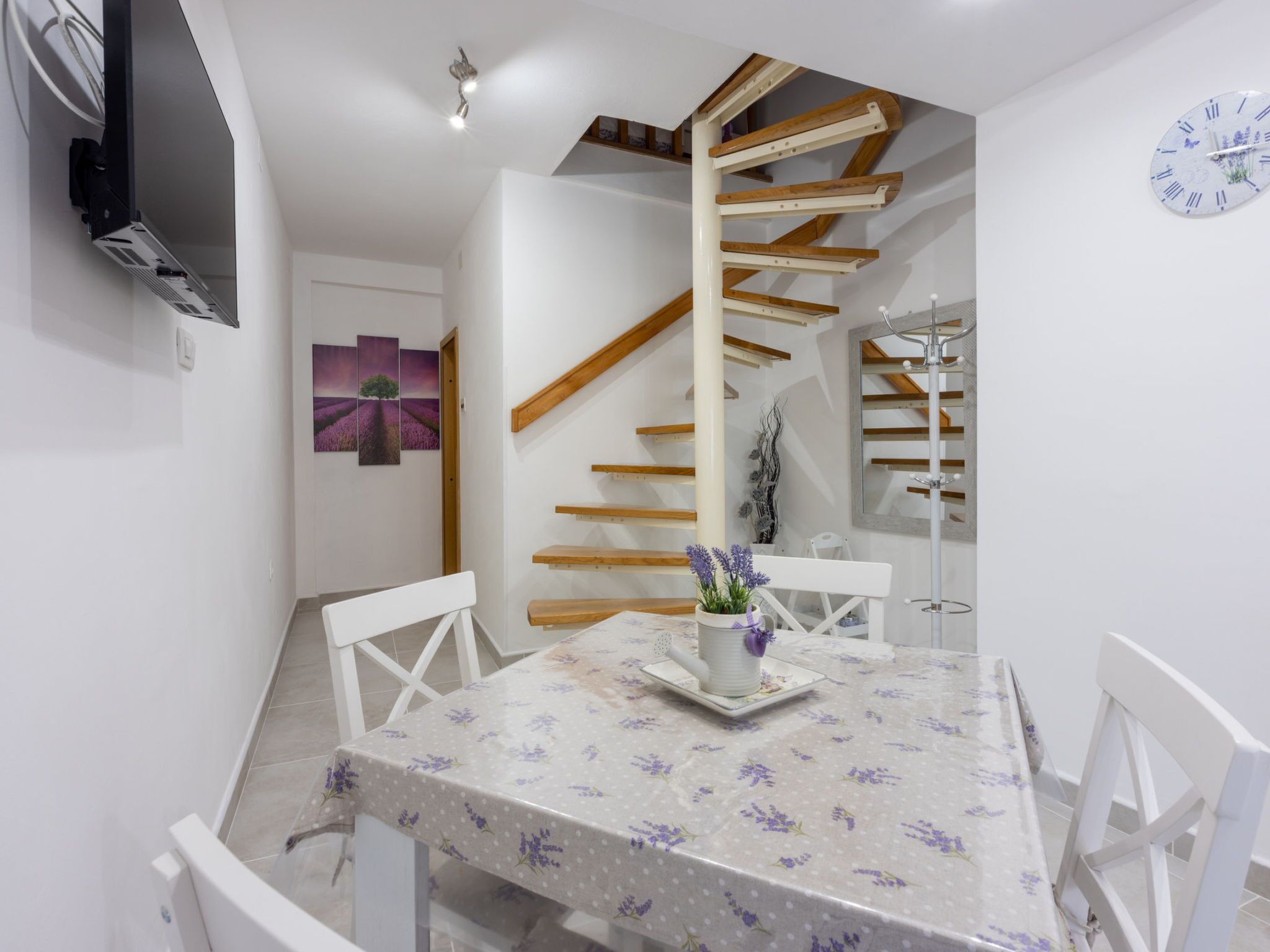 Ein Essbereich mit Tisch, Stühlen, einem Fernseher, einer Treppe und einer Uhr an der Wand.